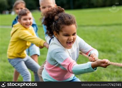 childhood, leisure and people concept - group of happy kids playing tug-of-war game and running at park. happy children playing tug-of-war game at park