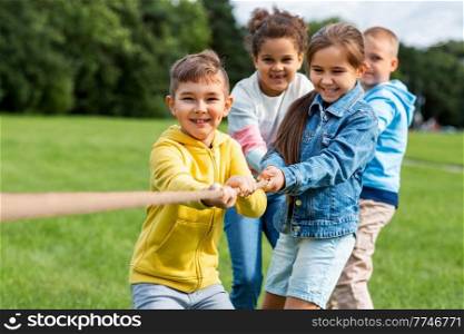 childhood, leisure and people concept - group of happy kids playing tug-of-war game and running at park. happy children playing tug-of-war game at park