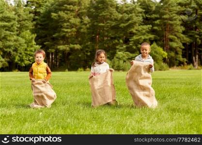 childhood, leisure and people concept - group of happy little children playing bag jumping game at park. happy children playing bag jumping game at park