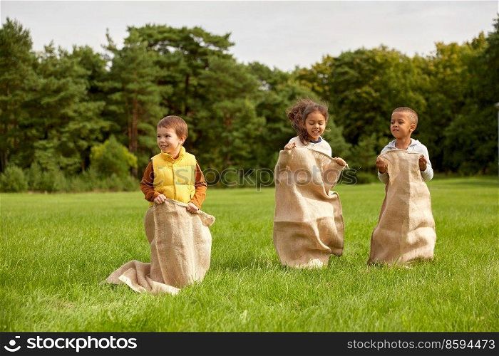 childhood, leisure and people concept - group of happy little children playing bag jumping game at park. happy children playing bag jumping game at park