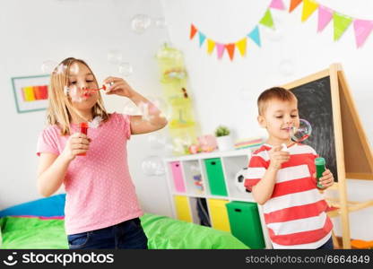 childhood, leisure and people concept - happy children blowing soap bubbles at home. happy children blowing soap bubbles at home