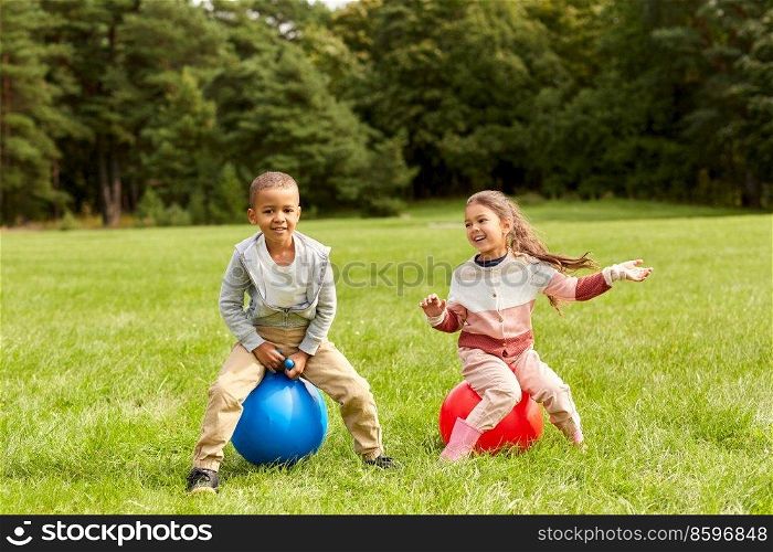 childhood, leisure and people concept - happy children bouncing on hoppers or bouncy balls at park. happy children bouncing on hopper balls at park