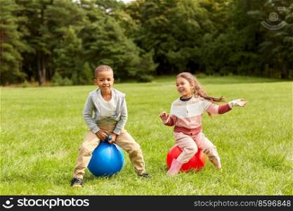 childhood, leisure and people concept - happy children bouncing on hoppers or bouncy balls at park. happy children bouncing on hopper balls at park