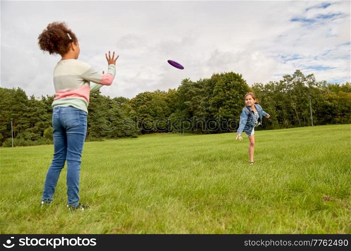 childhood, leisure and people concept - happy girls playing game with flying disc at park. happy girls playing with flying disc at park