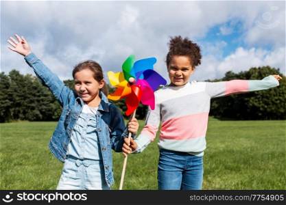 childhood, leisure and people concept - happy girls with pinwheel having fun at park. happy girls with pinwheel having fun at park