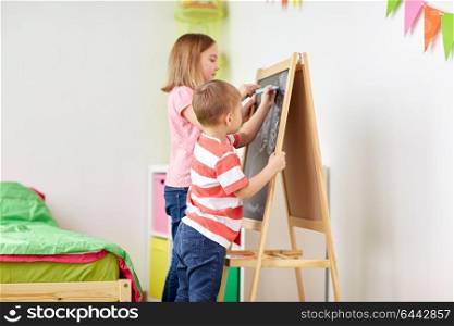 childhood, leisure and people concept - happy kids drawing on chalk board at home. happy kids drawing on chalk board at home