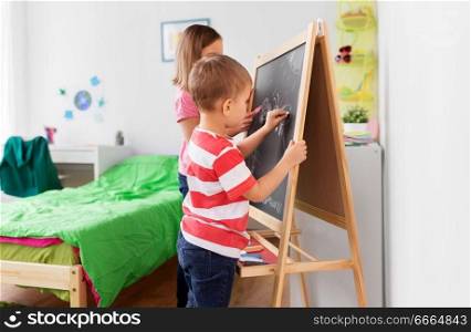 childhood, leisure and people concept - happy kids drawing on chalk board at home. happy kids drawing on chalk board at home