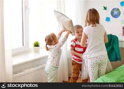 childhood, leisure and people concept - happy kids playing and fighting by pillows at home. kids playing and fighting by pillows at home