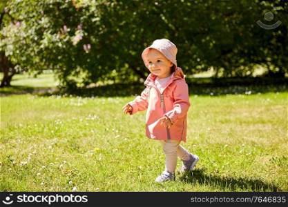 childhood, leisure and people concept - happy little baby girl in pink clothes walking at park in summer. happy little baby girl walking at park in summer