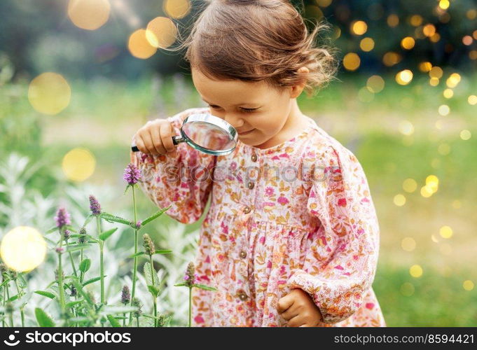 childhood, leisure and people concept - happy little baby girl with magnifier looking at flowers in summer garden. baby girl with magnifier looking at garden flowers