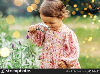 childhood, leisure and people concept - happy little baby girl with magnifier looking at flowers in summer garden. baby girl with magnifier looking at garden flowers