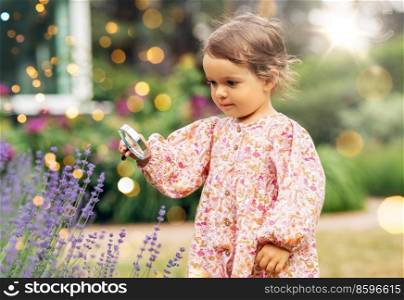 childhood, leisure and people concept - happy little baby girl with magnifier looking at lavender flowers in summer garden. baby girl with magnifier looking at garden flowers