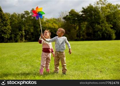 childhood, leisure and people concept - happy little boy and girl playing with pinwheel at park. happy children playing with pinwheel at park