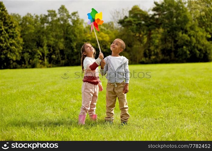 childhood, leisure and people concept - happy little boy and girl playing with pinwheel at park. happy children playing with pinwheel at park