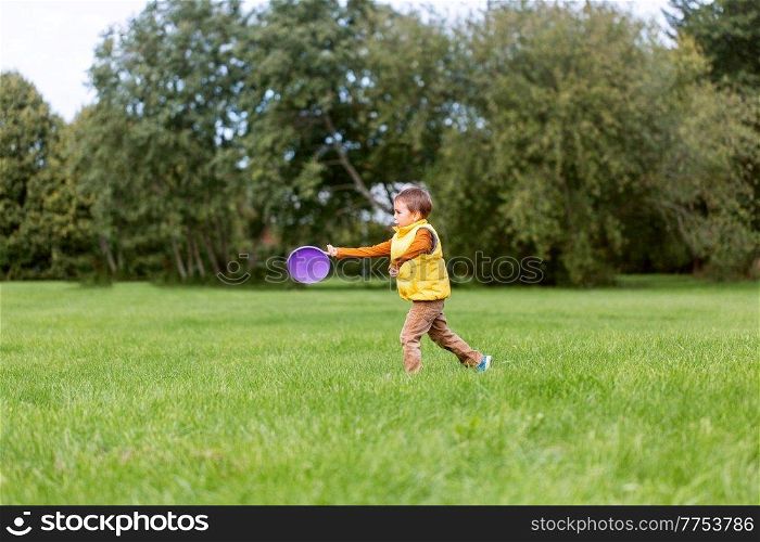 childhood, leisure and people concept - happy little boy playing game with flying disc at park. happy little boy playing with flying disc at park