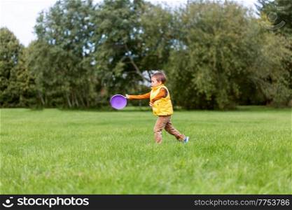 childhood, leisure and people concept - happy little boy playing game with flying disc at park. happy little boy playing with flying disc at park