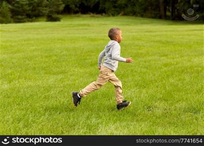 childhood, leisure and people concept - happy little boy running on green field at park. happy little boy running at park