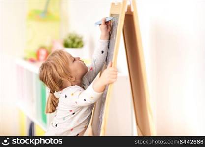 childhood, leisure and people concept - happy little girl drawing on chalk board at home. happy little girl drawing on chalk board at home