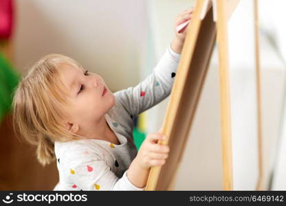 childhood, leisure and people concept - happy little girl drawing on chalk board at home. happy little girl drawing on chalk board at home