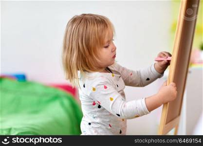 childhood, leisure and people concept - happy little girl drawing on chalk board at home. happy little girl drawing on chalk board at home