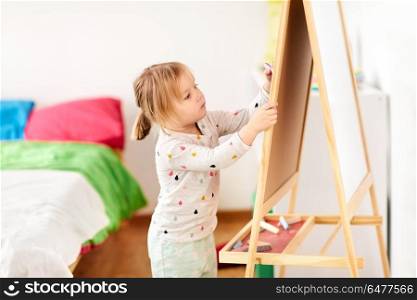 childhood, leisure and people concept - happy little girl drawing on chalk board at home. happy little girl drawing on chalk board at home. happy little girl drawing on chalk board at home