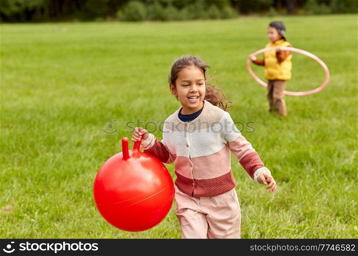 childhood, leisure and people concept - happy little girl playing with hopper ball at park. happy little girl playing with hopper ball at park