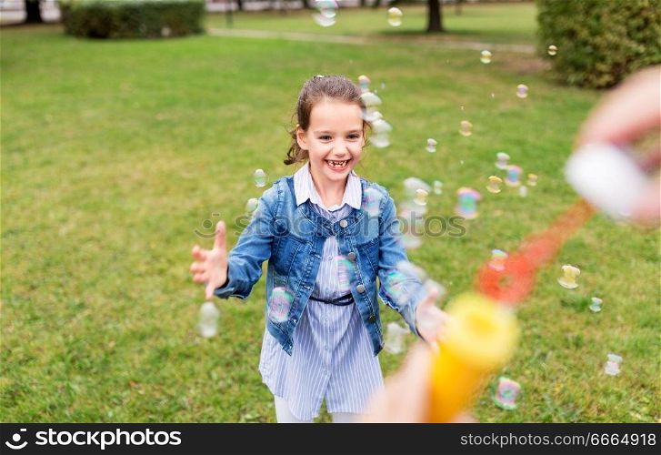 childhood, leisure and people concept - happy little girl playing with soap bubbles at summer park. happy girl playing with soap bubbles at park