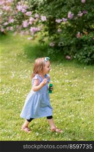 childhood, leisure and people concept - happy little girl with soap bubbles walking at summer park or garden. happy little girl with soap bubbles at summer park