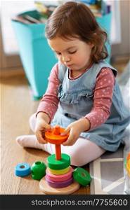 childhood, leisure and people concept - little baby girl playing with toy pyramid at home. happy baby girl playing with toy pyramid at home