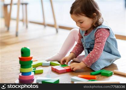 childhood, leisure and people concept - little baby girl playing with wooden toy blocks on floor at home. happy baby girl playing with toy blocks at home