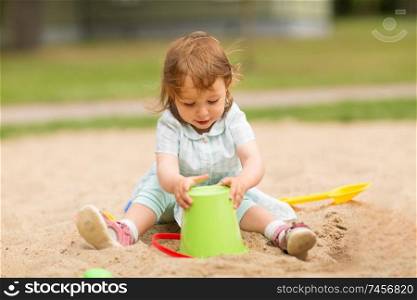 childhood, leisure and people concept - little baby girl plays with toys in sandbox. little baby girl plays with toys in sandbox
