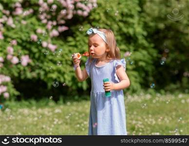 childhood, leisure and people concept - little girl blowing soap bubbles at summer park or garden. little girl blowing soap bubbles at park or garden