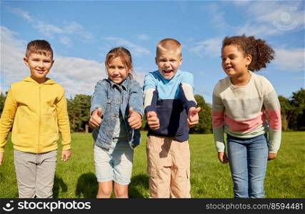 childhood, leisure and people concept - multiethnic group of happy kids showing thumbs up at park. happy children showing thumbs up at park