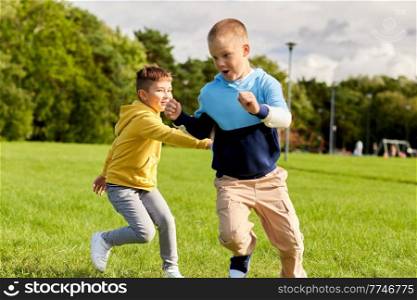 childhood, leisure and people concept - two happy boys playing tag game and running on lawn at park. two happy boys playing tag game at park