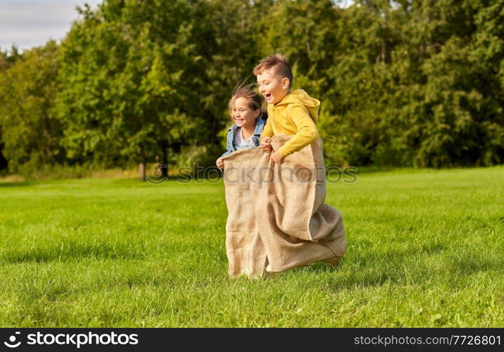 childhood, leisure and people concept - two happy children playing bag jumping game at park. happy children playing bag jumping game at park