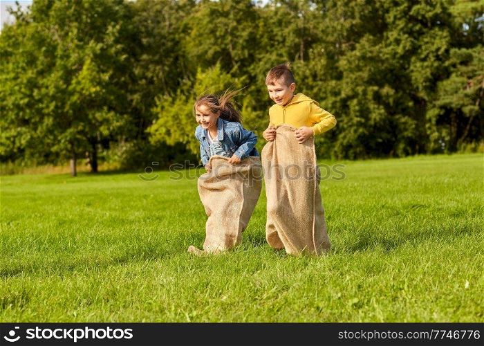 childhood, leisure and people concept - two happy children playing bag jumping game at park. happy children playing bag jumping game at park