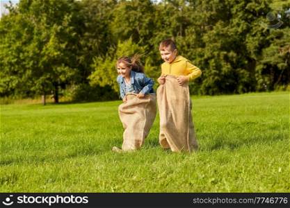 childhood, leisure and people concept - two happy children playing bag jumping game at park. happy children playing bag jumping game at park