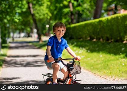 childhood, leisure and people - happy smiling little boy riding bicycle at summer park. happy little boy riding bicycle at summer park