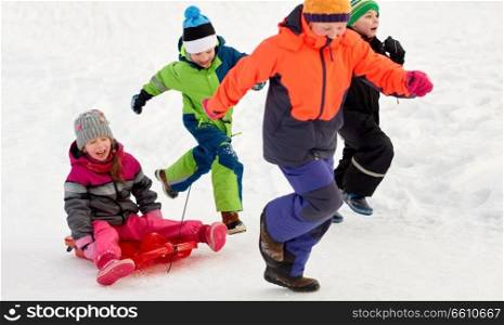 childhood, leisure and season concept - group of happy little kids in winter clothes with sled having fun outdoors. happy kids with sled having fun outdoors in winter