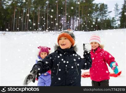 childhood, leisure and season concept - group of happy little kids in winter clothes playing snowball fight outdoors over snow and forest on background. happy little kids playing snowball fight in winter
