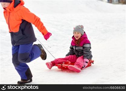 childhood, leisure and season concept - happy little girls in winter clothes with sled having fun outdoors. girls with sled having fun outdoors in winter