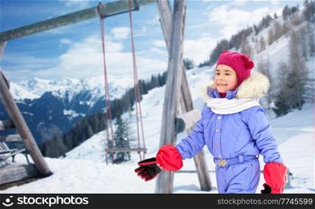 childhood, leisure and season concept - happy little girls in winter clothes outdoors over snow-covered mountains or alps and wooden swing on background. happy little girls in winter clothes outdoors