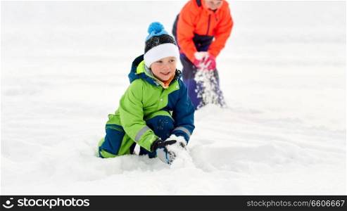 childhood, leisure and season concept - happy little kids in winter clothes playing with snow outdoors. happy little kids playing outdoors in winter