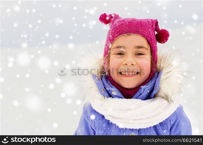 childhood, leisure and season concept - portrait of happy little girl in winter clothes outdoors over snow. happy little girl in winter clothes outdoors