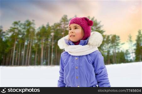 childhood, leisure and season concept - portrait of happy little girl in winter clothes outdoors over snowy forest or park background. happy little girl in winter clothes outdoors