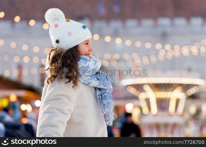 childhood, leisure and winter holidays concept - portrait of happy little girl over christmas market background. happy little girl at christmas market in winter
