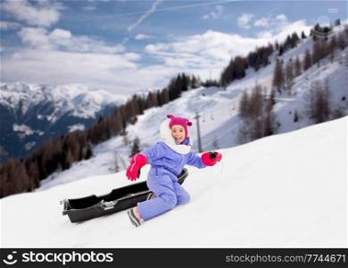 childhood, leisure and winter season concept - happy little girl with sled on snow hill over snow-covered mountains or alps on background. little girl with sled on snow hill in winter
