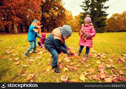 childhood, leisure, autumn, friendship and people concept - group of children collecting leaves in park