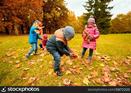 childhood, leisure, autumn, friendship and people concept - group of children collecting leaves in park