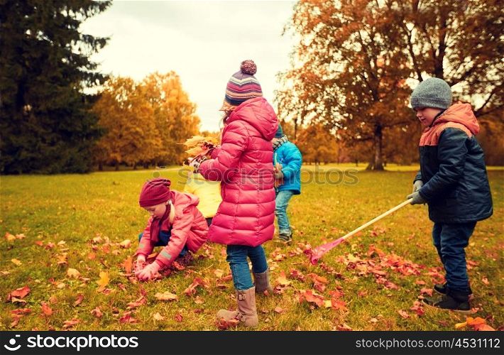 childhood, leisure, autumn, friendship and people concept - group of children with rack collecting and racking leaves in park